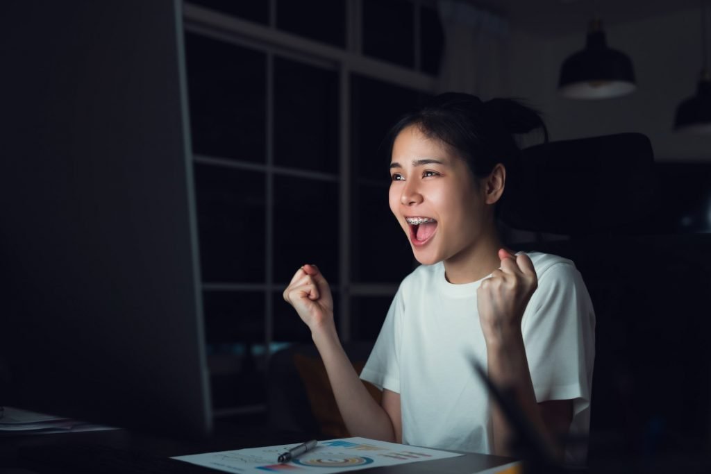 Happy excited Asian business woman celebrating success and working on computer at night.